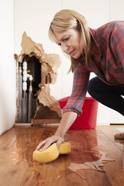 Stressed woman cleaning up water damage to her floor after burst pipe.